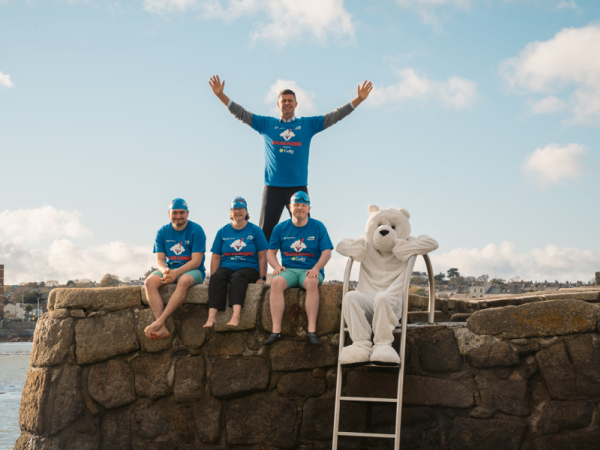 4 people and a large polar bear mascot stand beside water