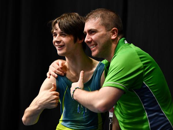 Coach with arm around smiling athlete with both giving a thumbs up sign