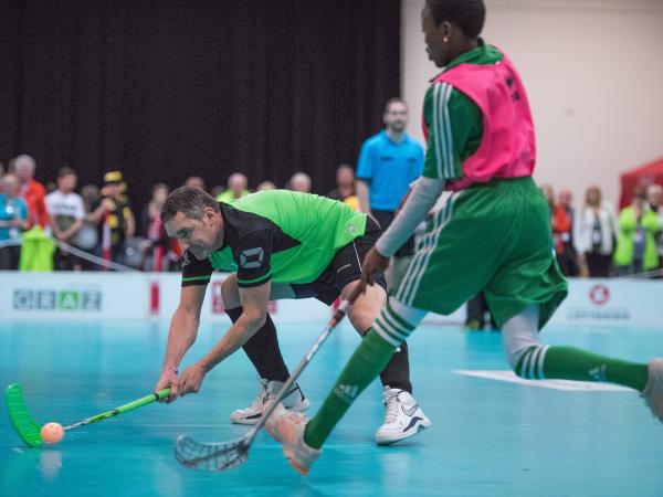 Floorball player striking ball past opponent with audience in background
