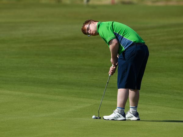 Special Olympics athlete holding golf club and putting on the green.