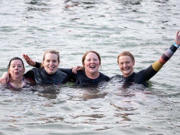 Four women laughing and smiling while doing polar plunge