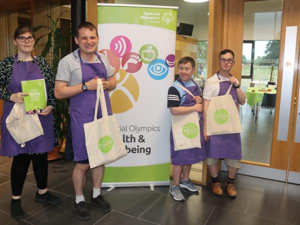 Athletes stand with goodie bags and banner for HEalthy Food Made Easy workshop