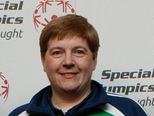 Woman in green and navy top smiles infront of Special Oylmpics Ireland backdrop