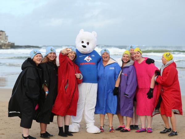 Seven women in dryrobes stand with polar bear mascot