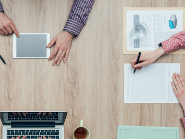 People's hands sitting at desk with laptopns and forms