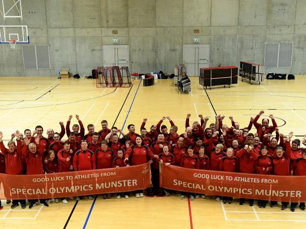 Group of over 100 people cheer towards the camera to celebrate Team Munster 