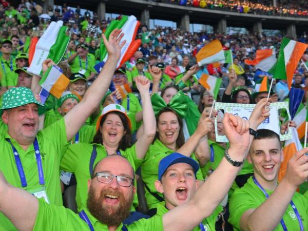 This image shows people in green tops at a match cheering and smiling waving around Irish flags.