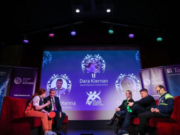 This image shows the stage at the 2026 Sport for Business event "Sporting Year Ahead". It features host Rob Hartnett interviewing three Special Olympics Ireland athletes in a round-table discussion format.
