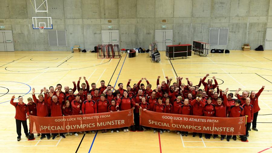Group of over 100 people cheer towards the camera to celebrate Team Munster 