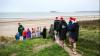 This image shows people walking down onto the beach to do the "Dip & Dine". With Santa hats on.