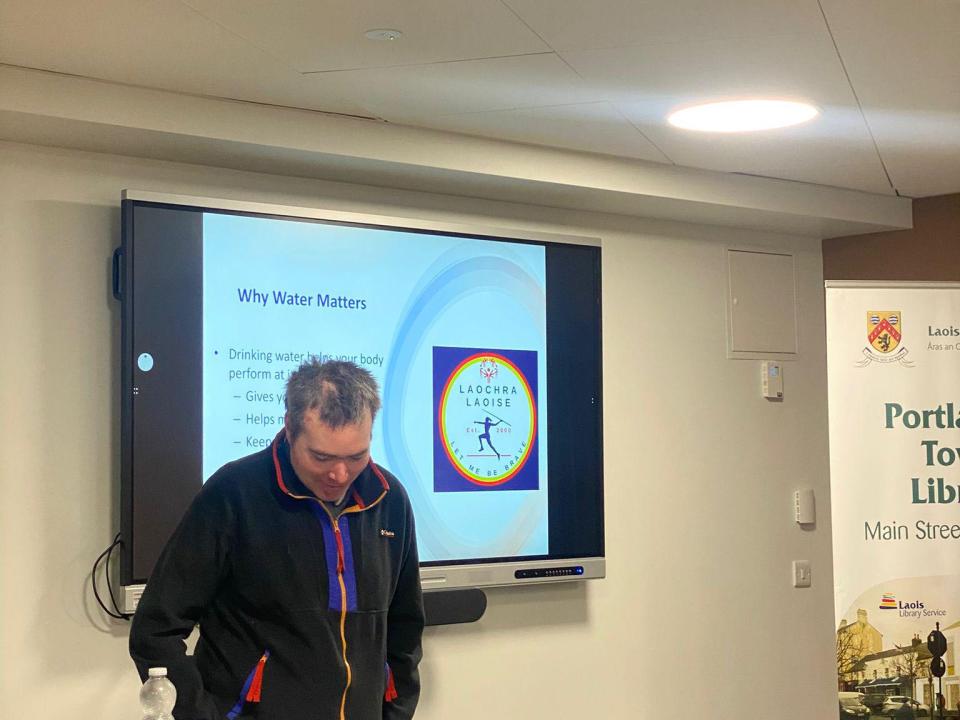 This image shows an athlete delivering a presentation about the importance of water