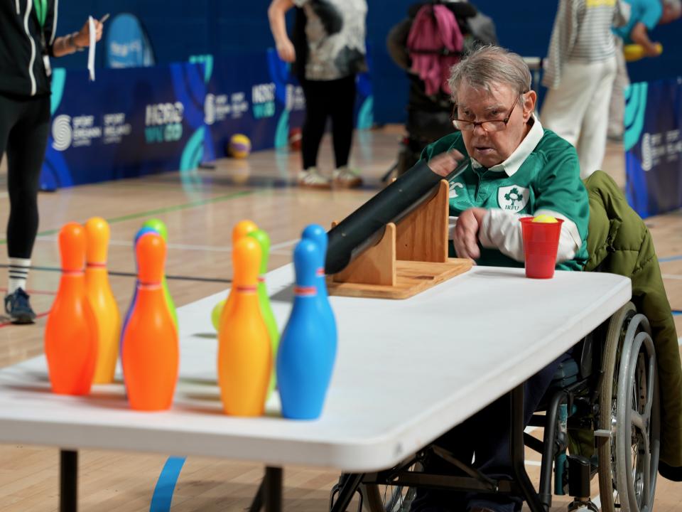This image shows an older male Motor Activities Training Program athlete performing an activity with a ball and bowling pins.