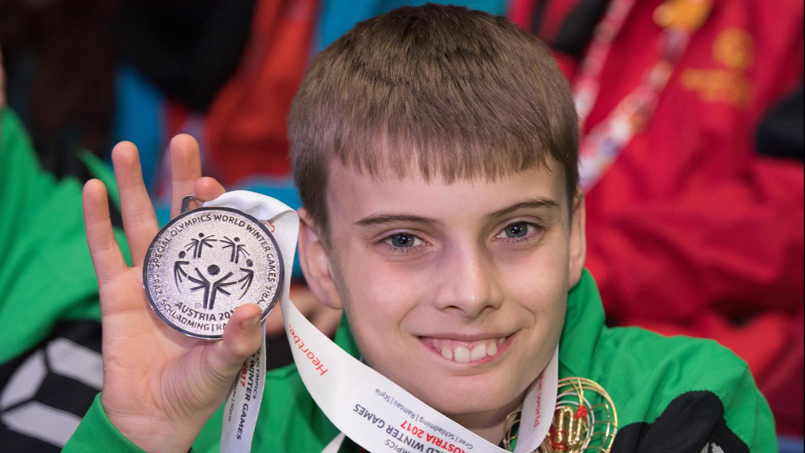 Young male athlete smiling and holding up medal