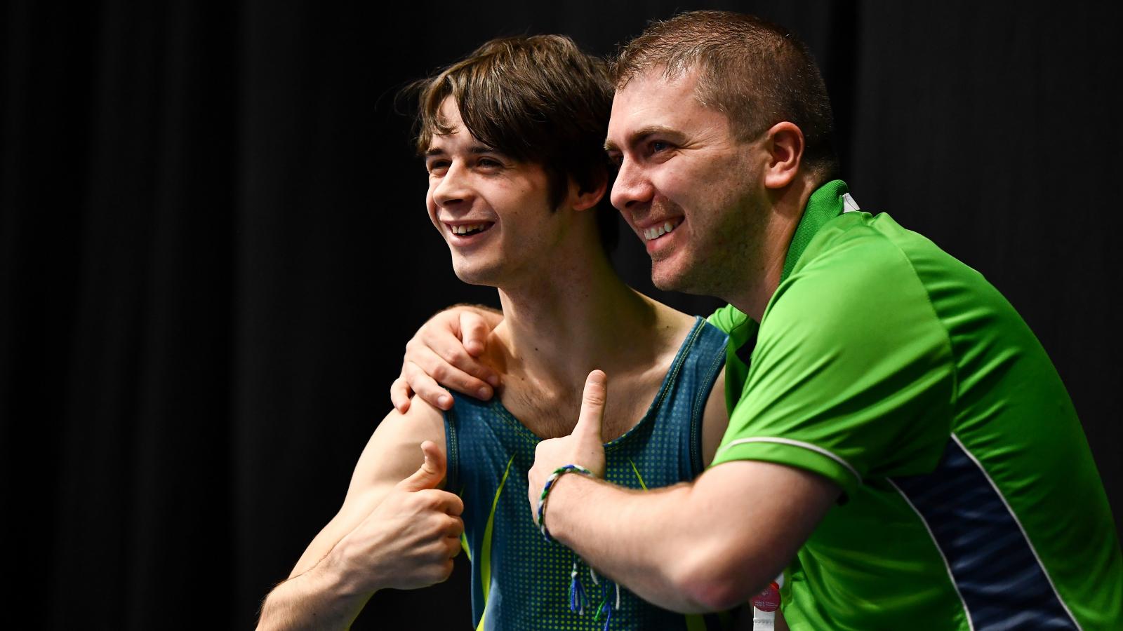 Coach with arm around smiling athlete with both giving a thumbs up sign