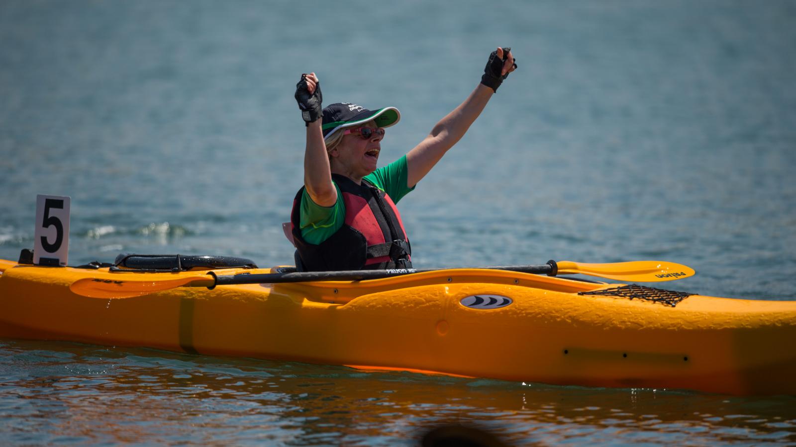 Athlete with arms raised in celebration whilst sitting in kayak