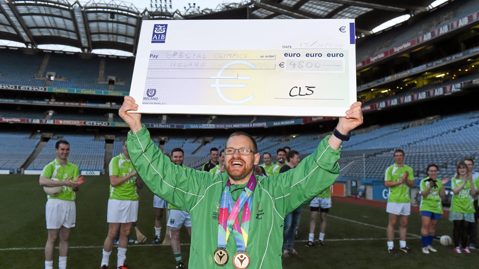 Male smiling athlete holding up a large cheque over his head.