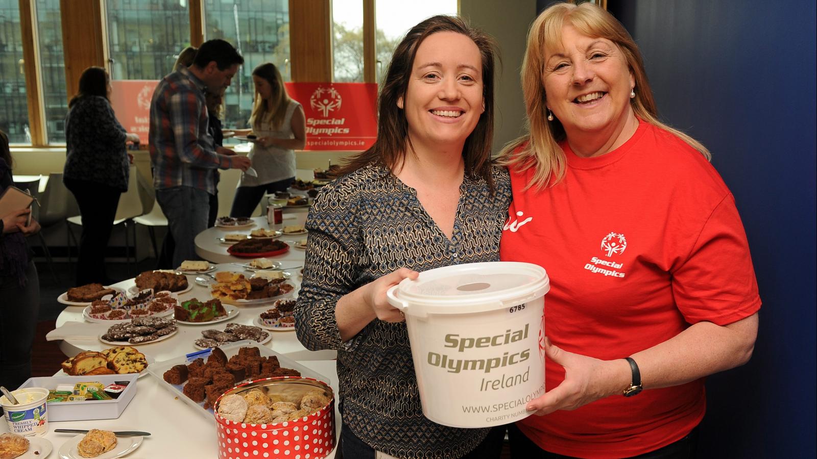Two fundraisers holding a collection bucket at a coffee morning in their workplace