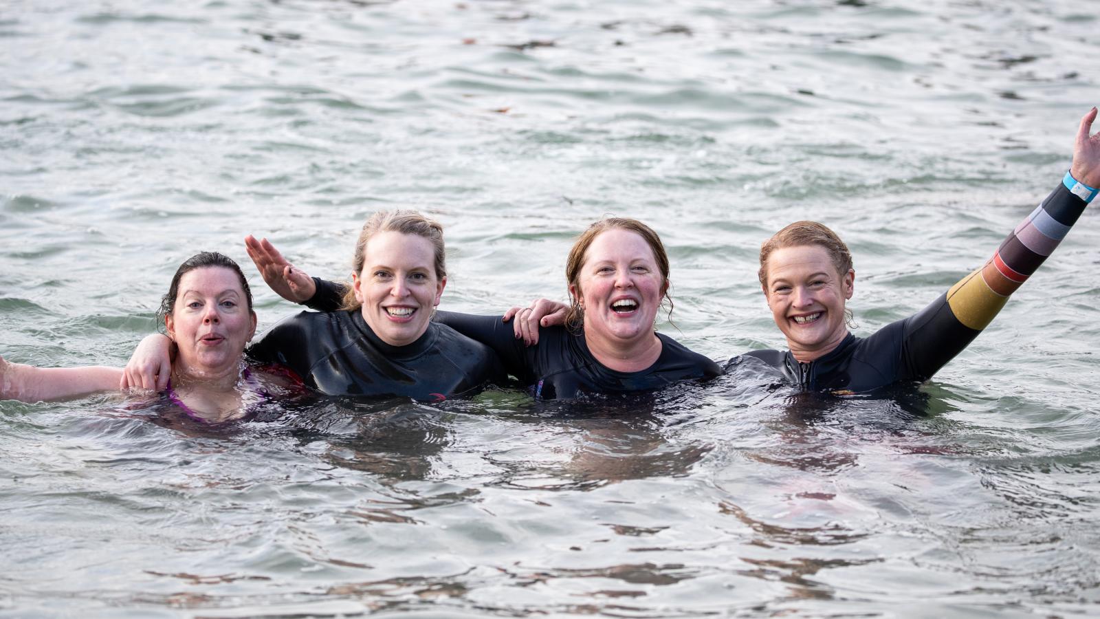 Four women laughing and smiling while doing polar plunge