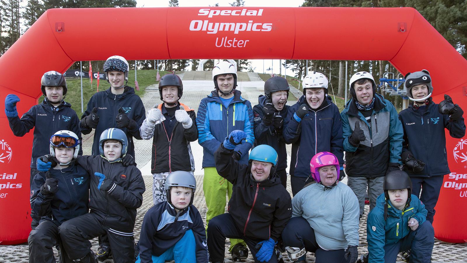 Team of skiers stand under arch and smile at camera