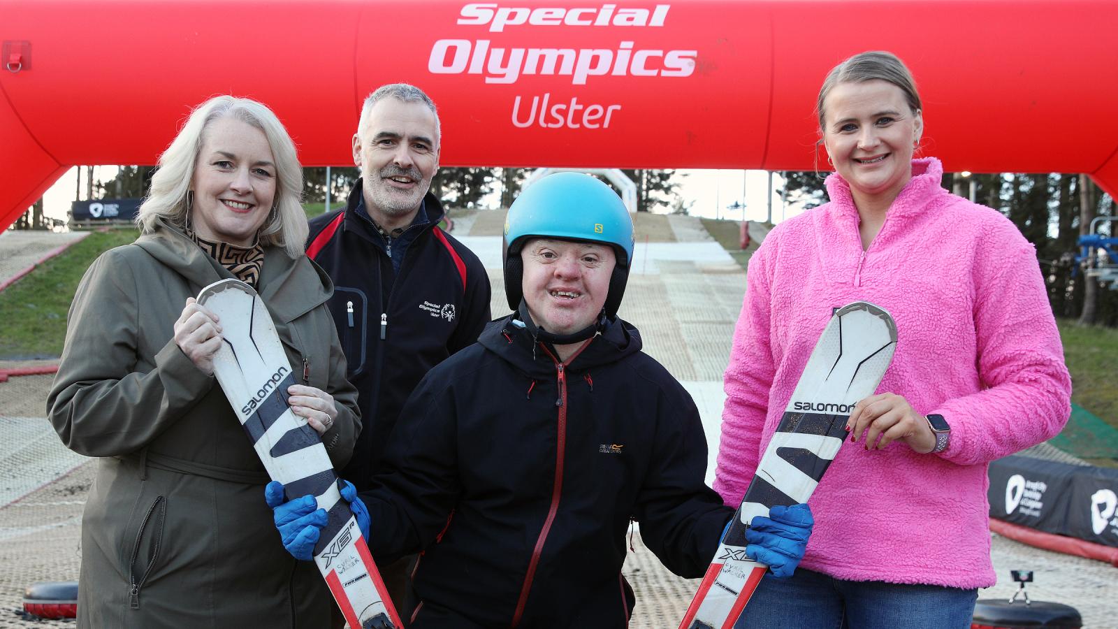 Four people stand on artifical ski slope and smile to camera